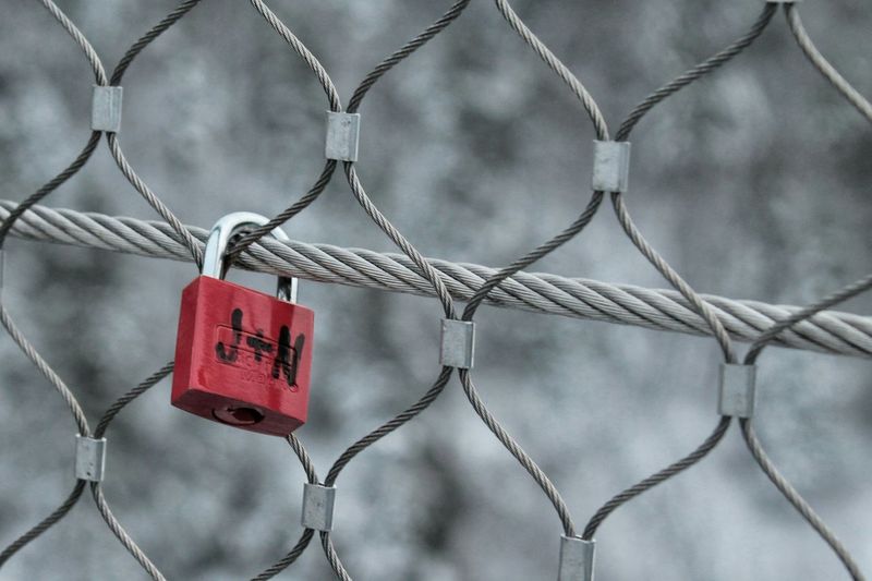 Close-up of red padlock on chainlink fence
