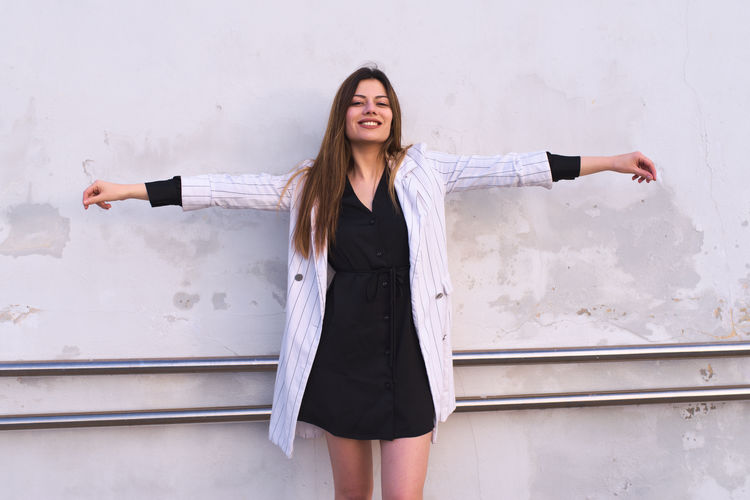 Happy young woman standing against wall