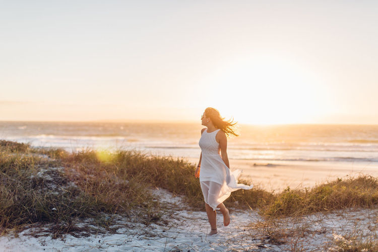 Young woman walking at beach against clear sky during sunset