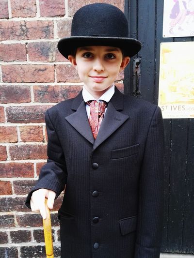 Boy wearing suit and hat standing against wall