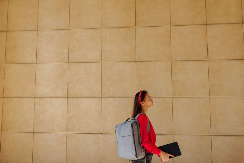 Side view of woman standing against wall outdoors