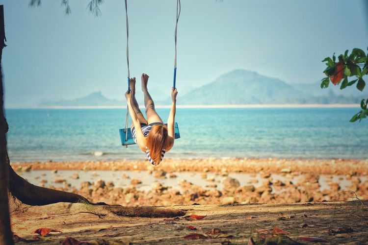 Rear view of woman swinging at on beach against sky