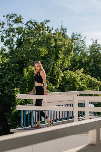 Side view of beautiful young woman standing on balcony against trees