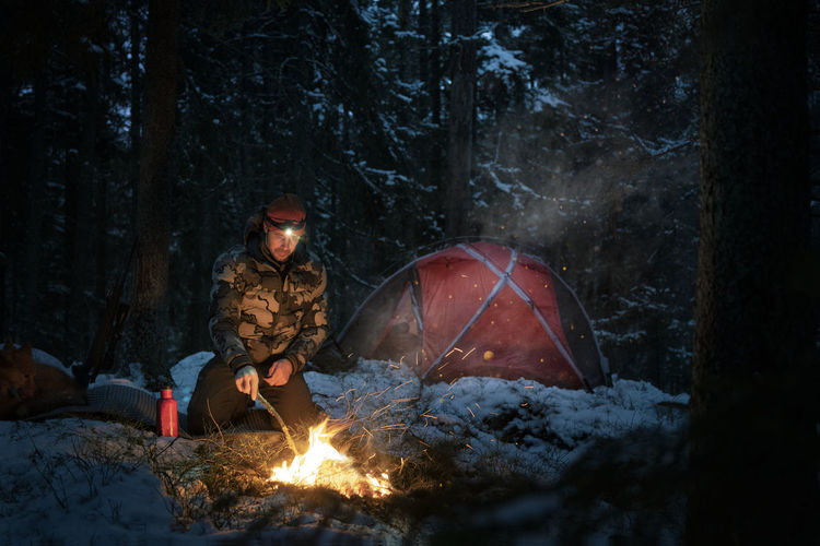Man at log fire in winter forest