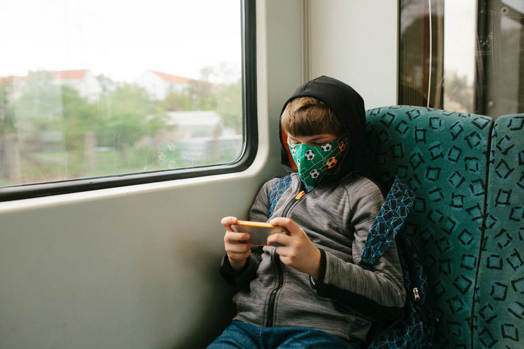Boy wearing mask while using phone during journey