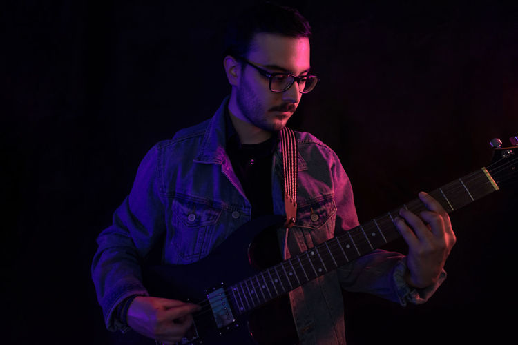 Young adult plays electric guitar under colored lights
