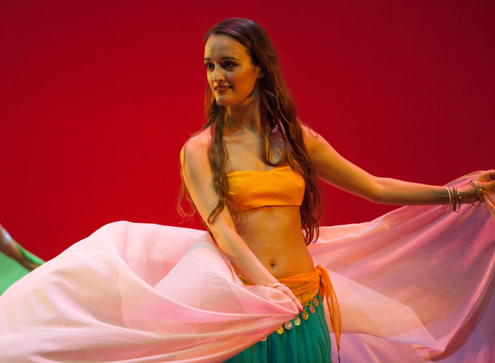 Smiling woman belly dancing against red background