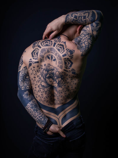 Rear view of shirtless man with tattoo standing against black background