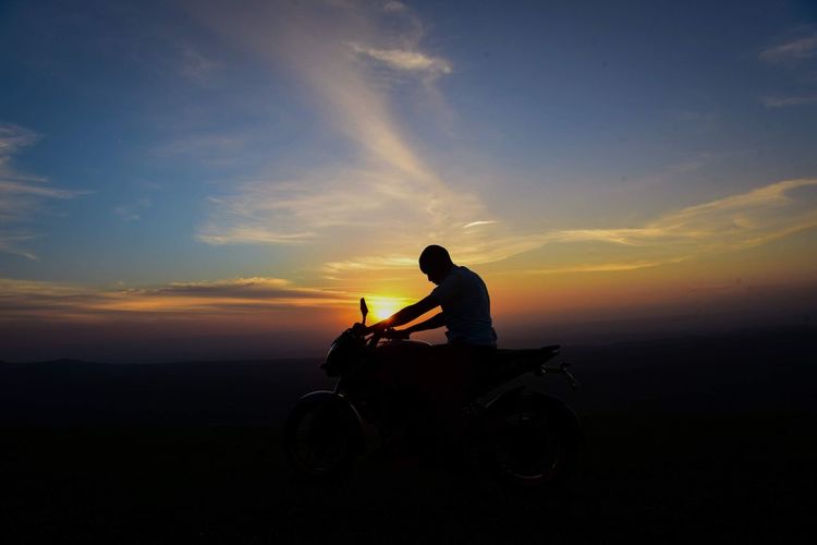 Silhouette man riding motorcycle against sky during sunset