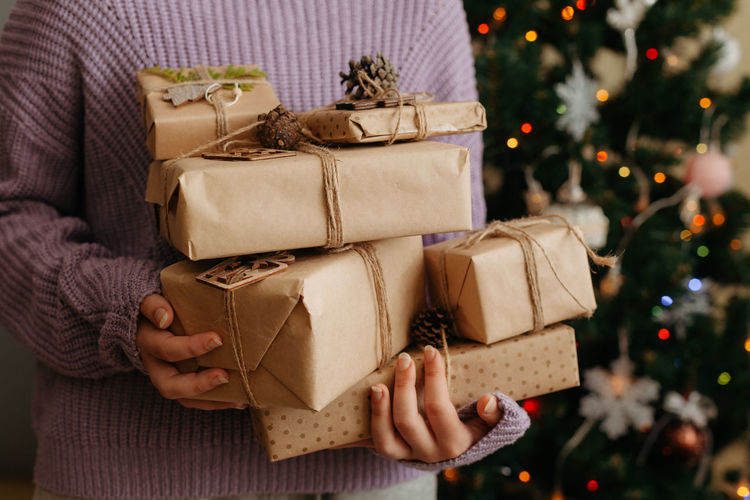 Closeup of woman in violet pullover holding many gift boxes in her hands. decorated christmas tree