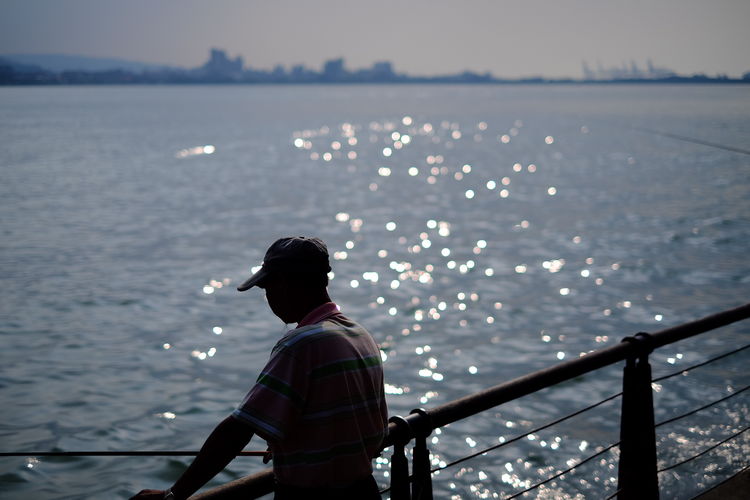 Man fishing standing by railing at harbor