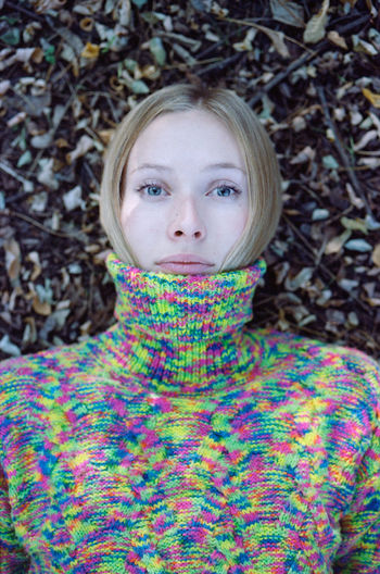 Close-up of a young woman in a sweater lying in the autumn forest.