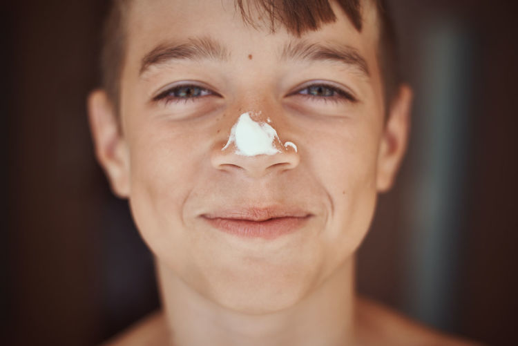 Close-up portrait of boy with suntan lotion on nose