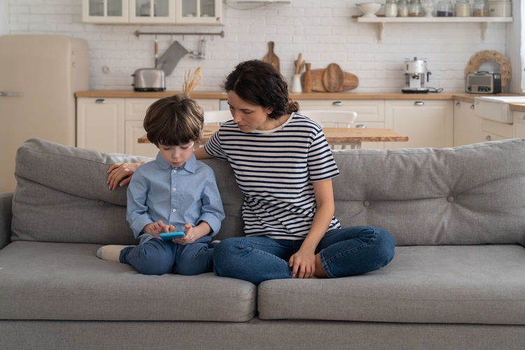 Son using mobile phone while sitting with mother at home