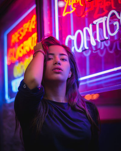 Portrait of woman standing against illuminated neon signs at night