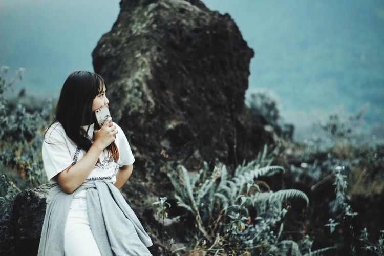 Young woman looking away while leaning on rock