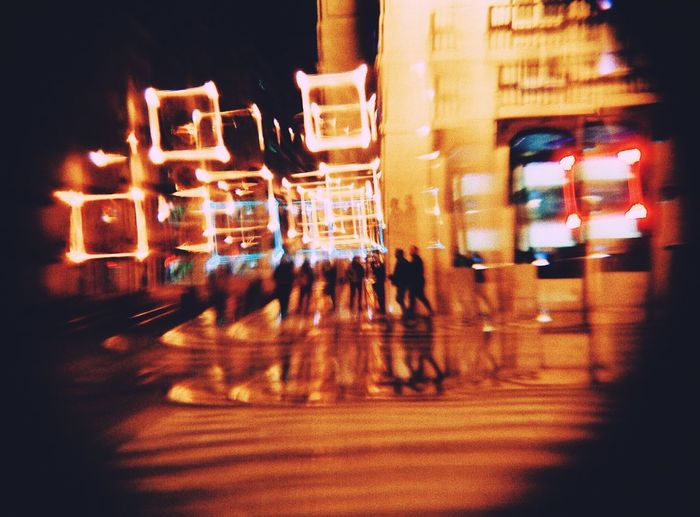 People walking on illuminated street against buildings at night