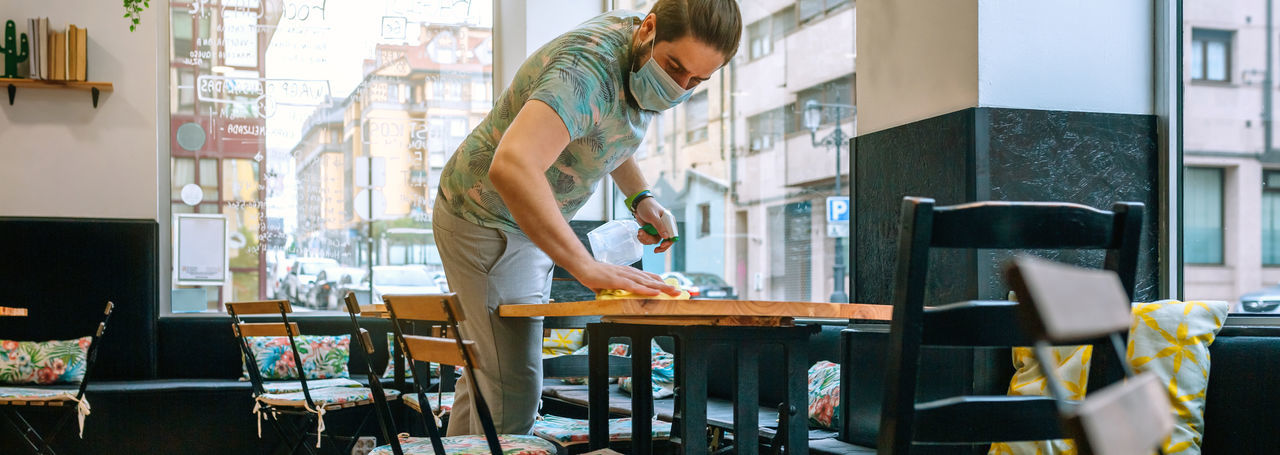 Man wearing mask cleaning table in cafe
