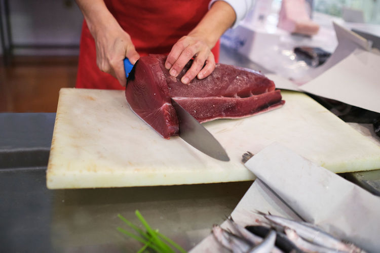 Young woman cuts up a red fish in her fishmonger's