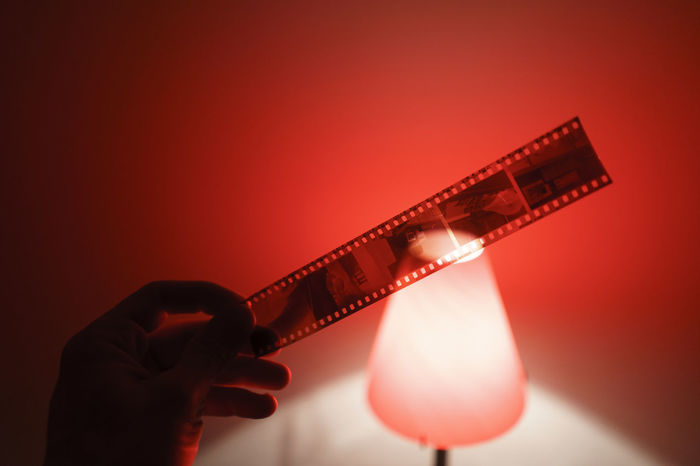Cropped hand holding film reel by illuminated lamp