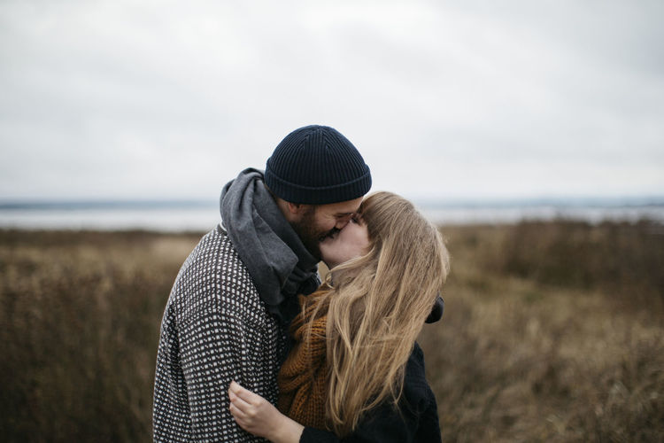Young couple standing on land against sea during winter