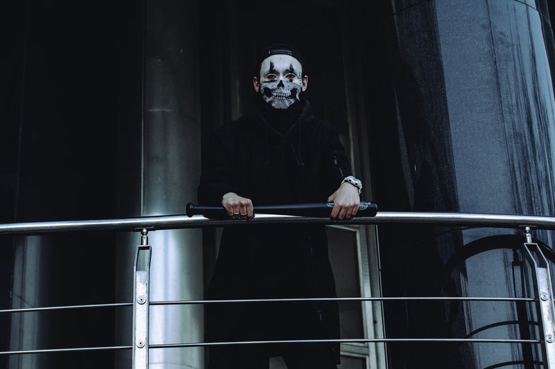 Low angle view of young man wearing mask standing by railing
