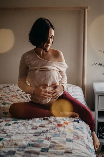 Pregnant woman on bed holding and looking at belly