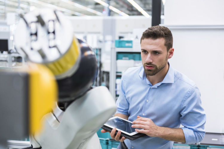 Man with tablet examining assembly robot in factory shop floor