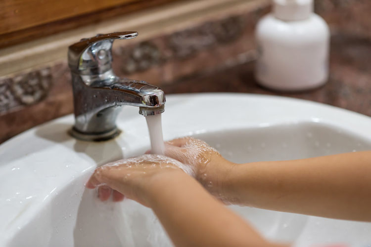 Child washing hand from faucet in bathroom to prevent covid-19