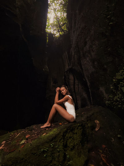 Full length of woman sitting on rock by cave