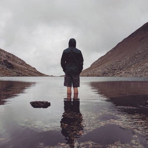 Rear view of man standing on lake against sky
