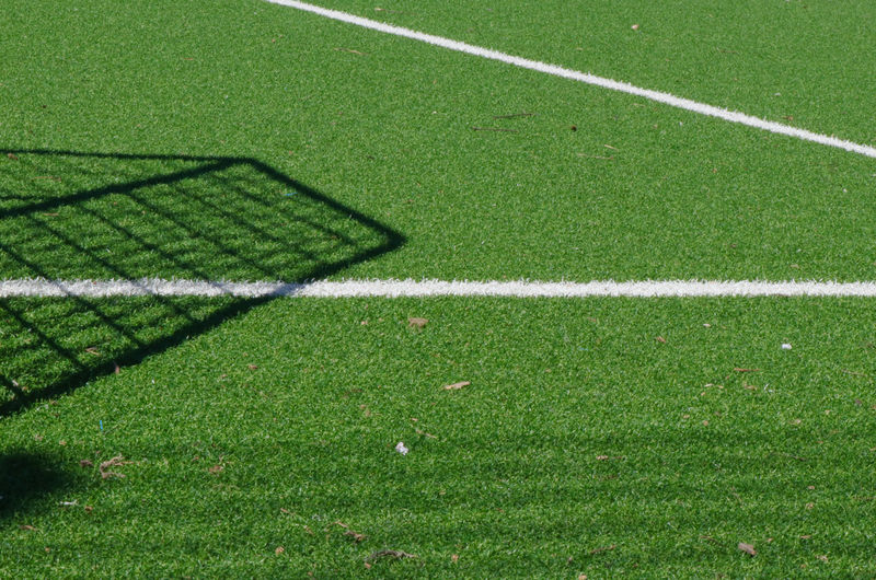 High angle view of green soccer field with white lines and shadow of goal