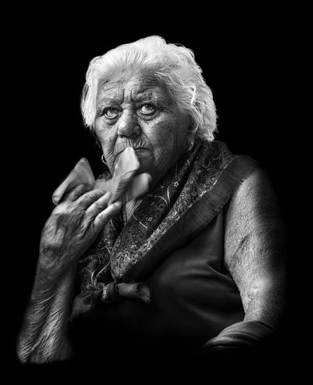 Senior woman looking away while sitting against black background