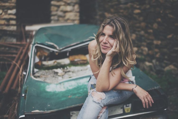 Woman sitting on abandoned car