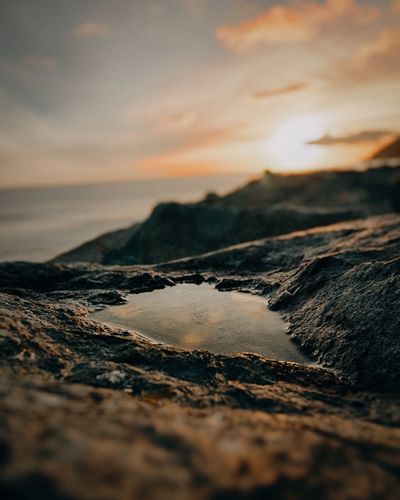Surface level of water on rock at beach against sky during sunset