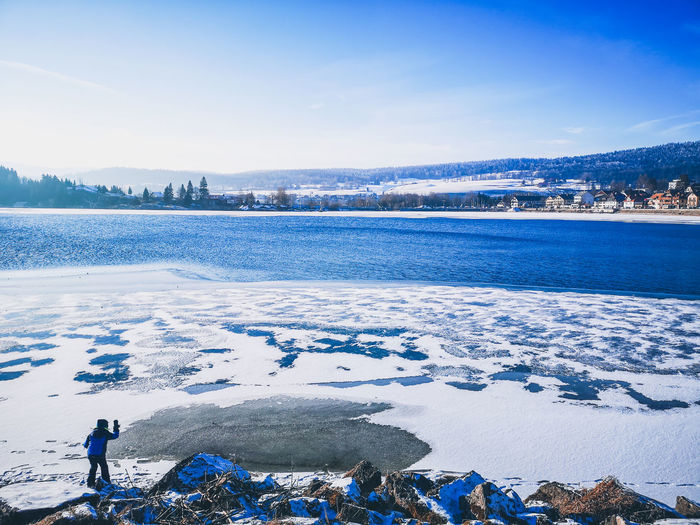 Scenic view of lake by snowcapped mountains against blue sky