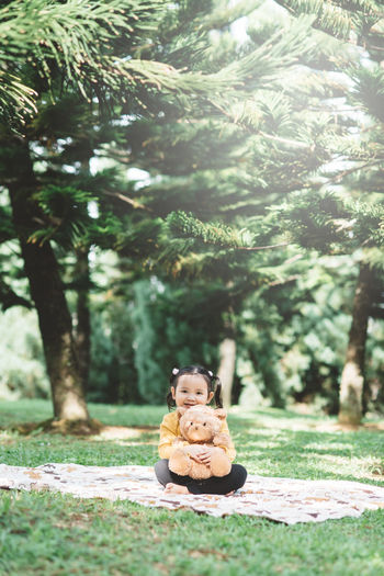 Portrait of girl sitting with teddy bear at park
