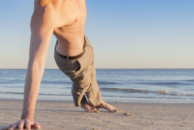 Low section of man exercising at beach against clear sky