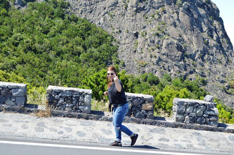 Full length portrait of woman showing obscene gesture while walking against mountains