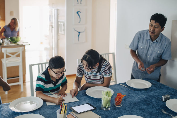 Teenage girl assisting boy in homework while father and sister standing at table