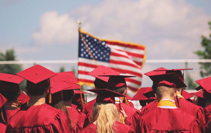 Rear view of graduates standing against american flag during sunny day
