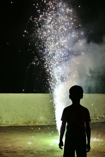 Rear view of boy burning cracker during diwali at night