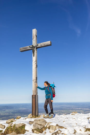 Germany, bavaria, female hiker standing in front of summit cross on hochries mountain