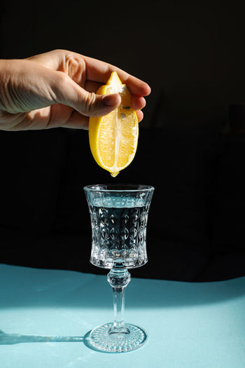 Close-up of hand holding lemon and squeezing it into glass of water