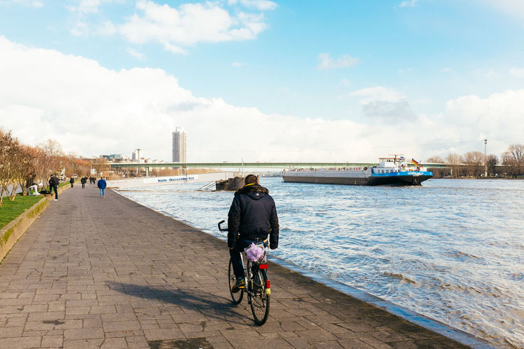 Rear view of man cycling on promenade by rhine river
