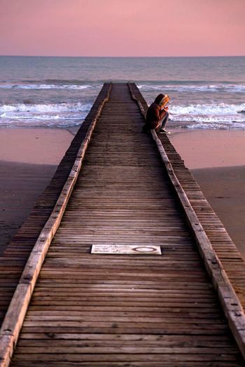 Woman sitting on wooden pier at beach during sunset