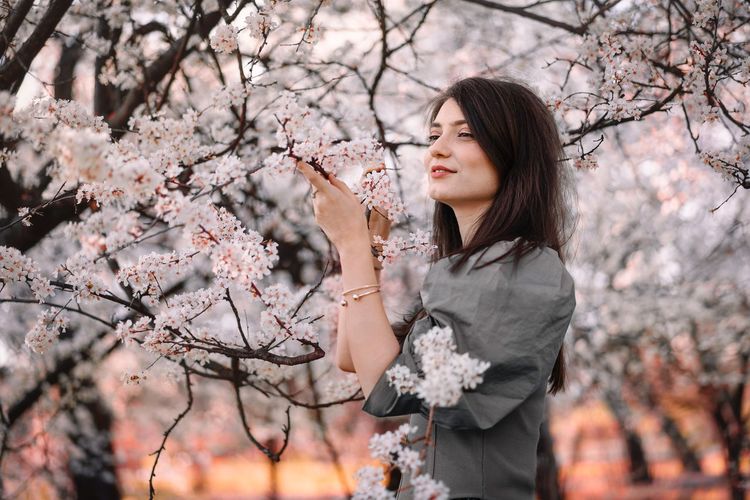  beautiful young woman standing by cherry blossom tree in spring