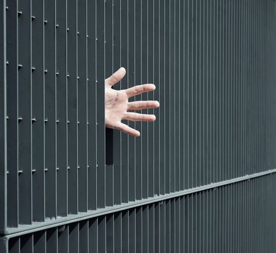 Cropped hand of man peeking from window
