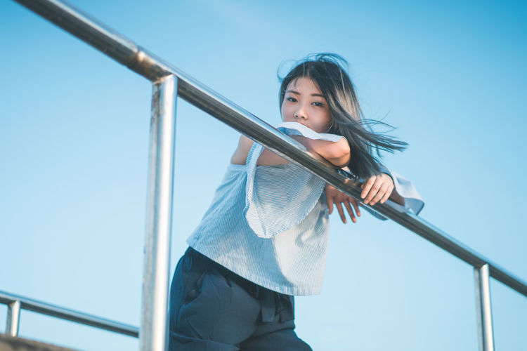 Portrait of young woman on footbridge against clear sky
