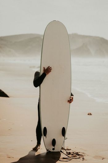 Man holding surfboard while standing on shore at beach